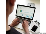 The image shows a person working on a laptop. The laptop is open and the screen is displaying a dashboard with various graphs...