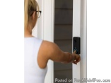 The image shows a woman's hand pressing a button on a door handle. She is wearing a white tank top and glasses. The door hand...