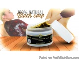 The image is an advertisement for a product called "100% Natural Black Soap". The product is in a white jar with a black lid....