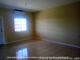 The image shows an empty room with a tiled floor and a window on the right side. The walls are painted in a light beige color...