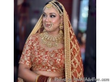 The image is a portrait of a beautiful Indian bride. She is wearing a traditional red and gold lehenga with intricate gold em...