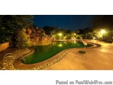 The image shows a beautiful outdoor swimming pool at night. The pool is rectangular in shape and has a curved edge. The water...