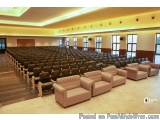 The image shows a large auditorium with rows of beige leather chairs arranged in neat rows. The chairs are facing towards the...