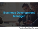 The image shows two men sitting at a desk in an office, engaged in a conversation. They are both wearing suits and appear to...