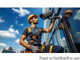 The image shows a construction worker wearing a hard hat and safety harness, holding a security camera attached to a window....