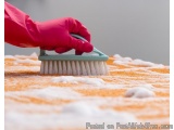The image shows a person's hand wearing a pink rubber glove holding a blue brush. The brush is being used to clean an orange...
