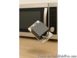The image shows a microwave oven with a black door and a silver handle. The door is open and there is a small black object at...