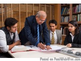 The image shows a group of four people, two men and two women, sitting around a table in a library or study area. They are al...