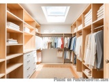This image shows a modern and spacious walk-in closet with wooden shelves and drawers. The closet has a skylight above the ce...