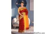 The image shows a woman wearing a traditional Indian saree. The saree is red in color with gold border and has a zari border....