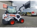 The image shows a Bobcat skid steer loader parked in front of a building. The loader is white with orange wheels and has a bl...