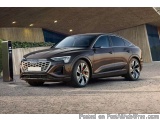 The image shows a dark brown Audi Q8 SUV parked in front of a modern building. The car is facing towards the left side of the...