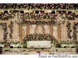 The image shows a beautiful and elegant wedding stage decorated with pink and white flowers and greenery. The stage is set up...