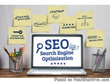 The image shows a laptop with the word "SEO" written on the screen in blue letters. The laptop is placed on a wooden desk wit...