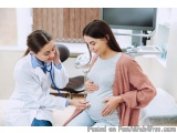 The image shows a pregnant woman sitting on a bed with a doctor standing next to her. The doctor is wearing a white coat and...