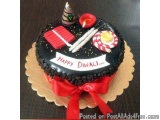 The image is of a Diwali cake. The cake is round and has a black base with a red ribbon tied around it. On top of the cake, t...