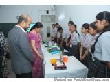 The image shows a group of young girls in school uniforms gathered around a table in a room. The table is covered with a whit...