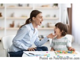 The image shows a mother and her young son sitting at a table in a living room. The mother is sitting on a white chair and th...