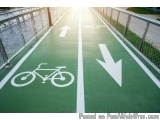 The image shows a green bicycle lane with white arrows pointing in different directions. The lane is located on a bridge with...