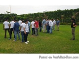The image shows a group of people standing in a line on a grassy field. They are all wearing casual clothes and appear to be...