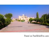 The image shows a large, well-manicured park with a clear blue sky in the background. In the center of the image, there is a...