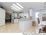 The image shows a modern kitchen with white cabinets and a large island in the center. The kitchen has a large window on the...
