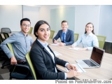 The image shows a group of four people sitting around a conference table in a meeting room. There are four people in the imag...