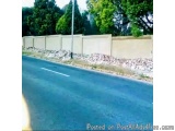 The image shows a street with a concrete wall on one side and a pile of rocks on the other side. The wall appears to be made...