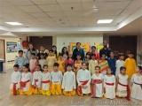 The image shows a group of children and adults posing for a group photo in a classroom. The children are dressed in tradition...