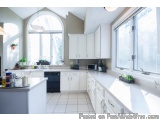 The image shows a modern kitchen with white cabinets and a large window on the right side. The kitchen has a large arched win...