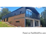 The image shows a modern two-story building with a black metal roof. The building is made of brick and has a large balcony on...