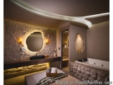 The image shows a modern bathroom with a curved ceiling. The walls are made of stone and there is a large round mirror on the...