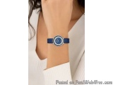 The image shows a close-up of a woman's wrist wearing a blue wristwatch. The watch has a round face with a white background a...