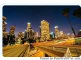 The image is a photograph of a city skyline at night. The sky is dark blue and the buildings are lit up with bright lights. T...
