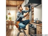 In this image, we can see a young man working in a modern kitchen. He is sitting on a ladder and is wearing a tool belt with...