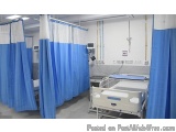The image shows a hospital room with a hospital bed in the center. The bed is white and has a blue mattress and headboard. On...
