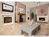 The image shows a modern living room with a large fireplace on the left side. The fireplace has a white mantel with a flat-sc...