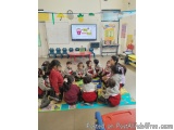 The image shows a group of children sitting on the floor in a classroom. They are all wearing school uniforms and are engaged...
