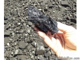 The image shows a hand holding a small piece of black rock. The rock appears to be a mineral or a mineral specimen, with a ro...