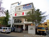 The image shows a modern building with a white exterior and red accents. The building is located on a street with other build...