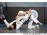 The image shows two men engaged in a martial arts fight. The man on the left is wearing a white judo uniform and is in a side...