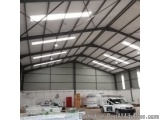 The image shows the interior of a large warehouse or industrial building with a high ceiling made of metal beams. The beams a...