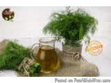 The image shows a glass pitcher of olive oil and a small glass jar filled with fresh green herbs. The jar is tied with a burl...