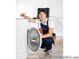 In this image, we can see a young man wearing a blue cap and overalls, kneeling on the floor in front of a washing machine. H...