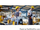 The image shows two workers in a factory setting. They are both wearing yellow hard hats and overalls and are standing in fro...