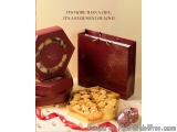 The image shows a red gift box with a gold lid and a handle on the right side. The box is open, revealing a small tray of coo...