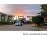 The image shows a beautiful sunset in a shopping mall. The sky is painted in a warm orange hue, with the sun setting in the b...