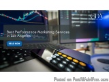 The image shows a desk with a laptop, a calculator, and a computer monitor. The laptop screen displays a stock market chart w...