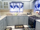 The image shows a modern kitchen with light blue cabinets and white countertops. The kitchen has a gas stove and oven on the...