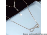 The image shows a gold necklace with a delicate chain. The necklace has a pendant in the shape of an infinity symbol with sma...